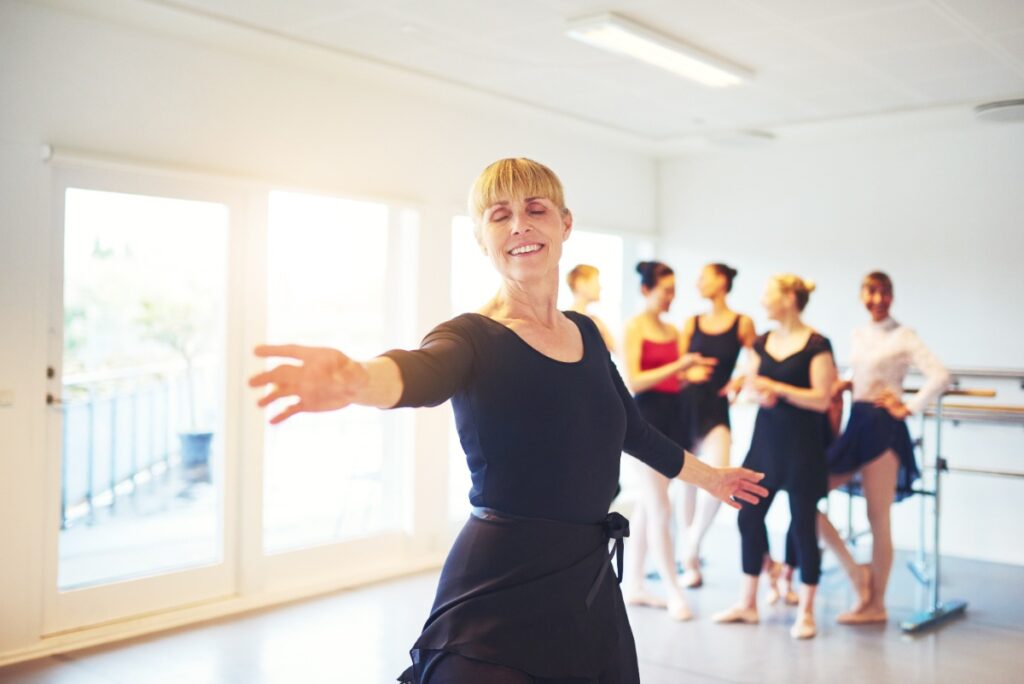 Une femme répète une chorégraphie devant un miroir, sourire aux lèvres, tenue de danse noire ajustée