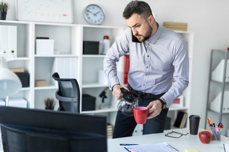 Un jeune homme qui téléphone dans son bureau et tient un tas de café
