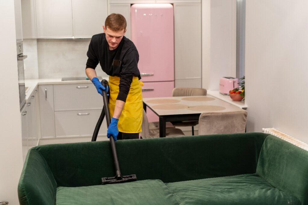 Un homme portant un tablier et nettoie le canapé avec un aspirateur